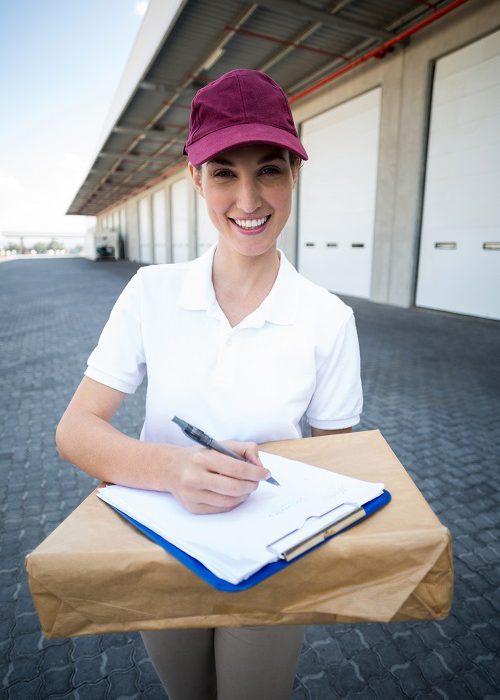 Portrait of delivery woman holding a clipboard and parcel outside the warehouse
